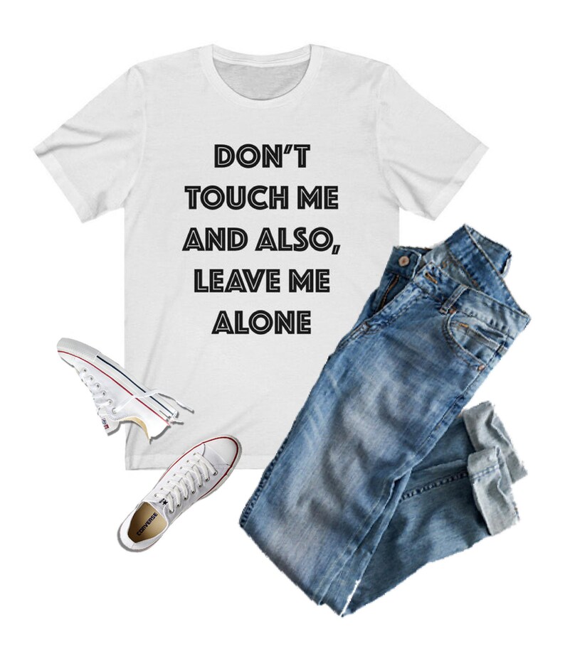 May include: White t-shirt with black text that reads "Don't touch me and also, leave me alone". The shirt is paired with blue jeans and white sneakers.