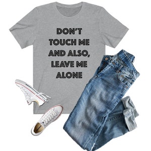 May include: A gray t-shirt with the text "DON'T TOUCH ME AND ALSO, LEAVE ME ALONE" printed in black.