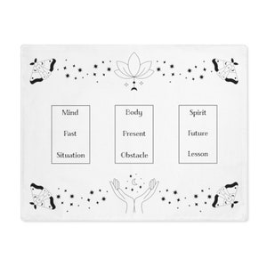 Puede incluir: Un paño de tarot blanco con dibujos de línea negra de polillas, estrellas, manos, una flor de loto y una luna creciente. El paño está dividido en tres secciones etiquetadas como "Mente", "Cuerpo" y "Espíritu". Cada sección tiene tres sub-etiquetas: "Pasado", "Presente", "Futuro", "Situación", "Obstáculo" y "Lección".