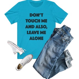 May include: A turquoise blue t-shirt with the text "Don't touch me and also, leave me alone" printed in black.