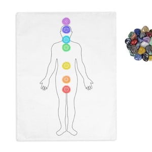 May include: A white towel with a black outline of a human figure with seven colored circles representing the seven chakras. The chakras are located at the crown, third eye, throat, heart, solar plexus, sacral, and root chakras. The towel is next to a pile of colorful gemstones.
