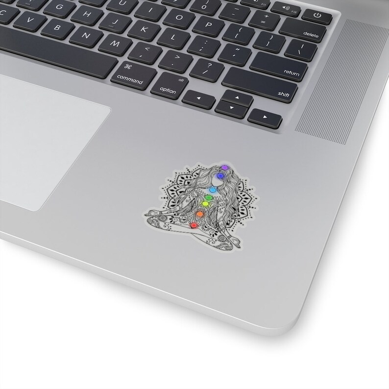 May include: A black and white illustration of a woman sitting in a lotus position with a mandala behind her. The woman has seven chakras represented by colored circles on her body.