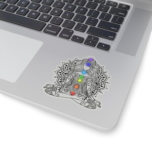 May include: A black and white illustration of a woman sitting in a lotus position with a mandala behind her. The woman has seven chakras represented by colored circles on her body.