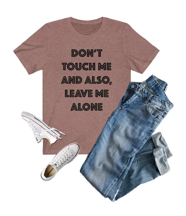 May include: A heather brown t-shirt with the text "Don't touch me and also, leave me alone" in black. The shirt is paired with blue jeans and white sneakers.