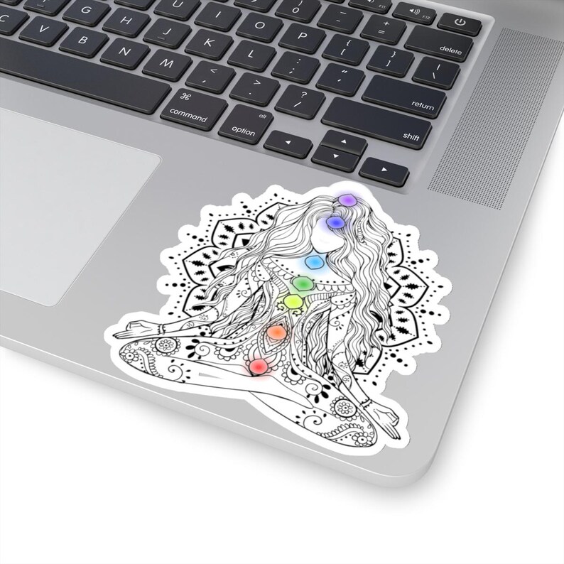 May include: Black and white line art illustration of a woman in a yoga pose with a mandala behind her. The woman has seven colorful chakras, representing the seven energy centers of the body.