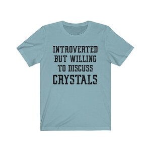 May include: A light blue t-shirt with the text "Introverted but willing to discuss crystals" printed in black.