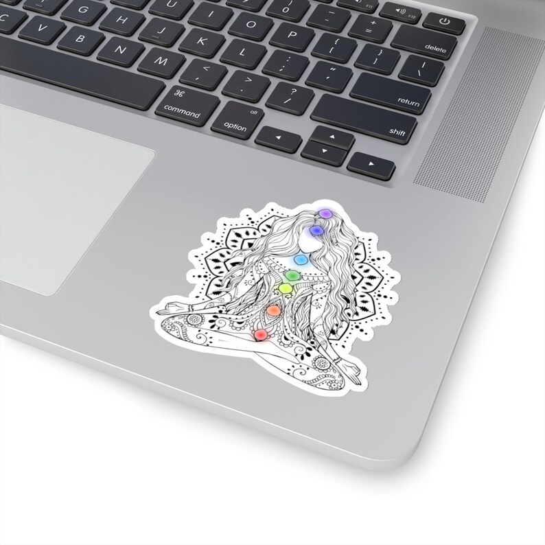 May include: A black and white line drawing of a woman in a yoga pose with seven colorful chakras. The woman is surrounded by a mandala design.