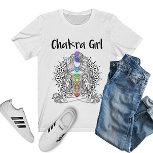 May include: White t-shirt with the text "Chakra Girl" and a black and white illustration of a woman in a yoga pose with colorful chakras.