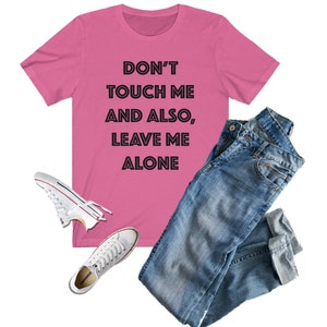 May include: Pink t-shirt with the text "DON'T TOUCH ME AND ALSO, LEAVE ME ALONE" in black outlined letters.
