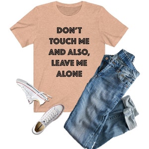 May include: A peach-colored t-shirt with the text "DON'T TOUCH ME AND ALSO, LEAVE ME ALONE" printed in black.