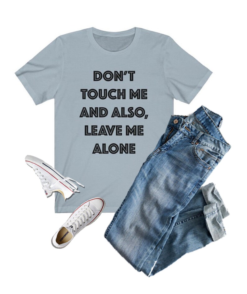 May include: A light blue t-shirt with the text "DON'T TOUCH ME AND ALSO, LEAVE ME ALONE" in black. The shirt is paired with blue jeans and white sneakers.