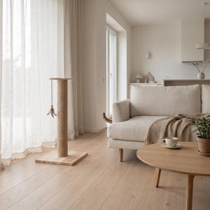 May include: A cylindrical cat scratching post with a light-colored wooden square base and a sisal-wrapped column. A small dangling toy with feathers is attached to the top of the post, which stands upright on a light-toned wooden floor.