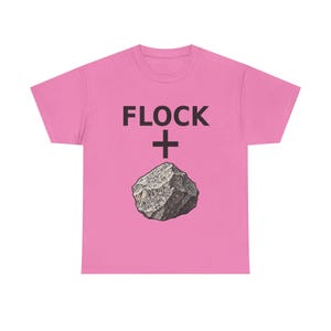 Może przedstawiać: Jasnoróżowy t-shirt z krótkim rękawem, z czarnym napisem FLOCK, czarnym znakiem plusa oraz szczegółową ilustracją szarego, nakrapianego kamienia umieszczoną na środku przodu odzieży.