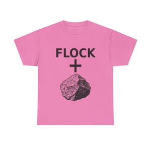 Puede incluir: Una camiseta de manga corta de color rosa brillante con el texto negro FLOCK seguido de un signo más negro y una ilustración gráfica negra de una roca centrada en la parte delantera de la prenda. El diseño está impreso en una fuente negrita.
