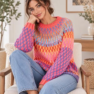 Può includere: Un maglione in maglia a maniche lunghe con un vivace motivo a scacchi nei toni del corallo, rosa, arancione e azzurro. Il maglione presenta uno scollo rotondo, polsini a coste e un orlo a coste, abbinato a jeans in denim azzurro.