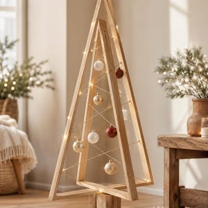 Può includere: Una struttura triangolare per albero di Natale realizzata in legno chiaro, con una base a blocco solido. Il telaio è decorato con sottili luci a filo e diversi ornamenti rotondi nei toni del bianco, oro e rosso scuro, sospesi da fili sottili.