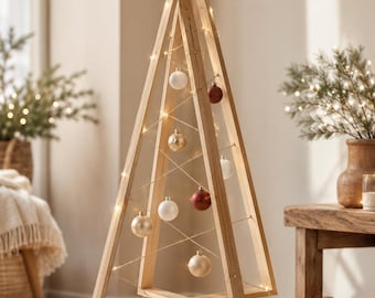 Könnte beinhalten: Ein dreieckiger Weihnachtsbaum aus hellem Holz mit einem massiven Sockel. Der Rahmen ist mit einer dünnen Lichterkette und mehreren runden Kugeln in Weiß, Gold und Dunkelrot geschmückt, die an feinen Drähten im Inneren des Rahmens hängen.