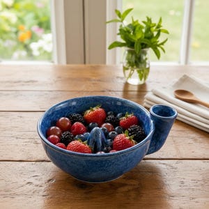 Könnte beinhalten: Eine blaue Keramikschale für Beeren mit gesprenkelter Oberfläche und einem zentralen Abflusskegel, gefüllt mit frischen Erdbeeren, Brombeeren und Weintrauben. Die Schale hat einen kleinen seitlichen Griff zum Waschen und Servieren.
