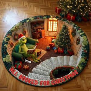 Puede incluir: Una alfombra redonda con una ilustración en 3D de una criatura verde con gorro de Papá Noel sentada en un sofá verde leyendo un libro. La escena incluye un árbol de Navidad, regalos, una estantería y escaleras. El texto dice DAVID y ALL BOOKED FOR CHRISTMAS.