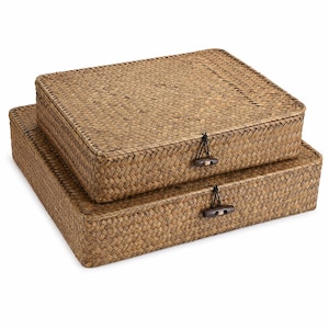 May include: Two rectangular storage boxes crafted from woven brown seagrass material. Each box features a flat lid and a toggle closure consisting of a dark brown wooden button attached by a black cord loop to secure the lid in place.