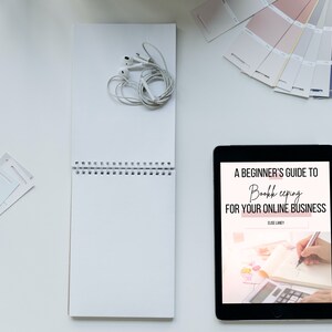May include: A tablet displaying an ebook cover titled "A Beginner's Guide to Bookkeeping for Your Online Business" by Elise Landry. The cover features a hand writing in a notebook with a calculator nearby.