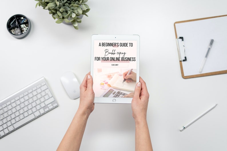 May include: A white tablet displaying a pink and white ebook cover with the title "A Beginner's Guide to Bookkeeping for Your Online Business". The cover features a hand writing in a notebook with a calculator.