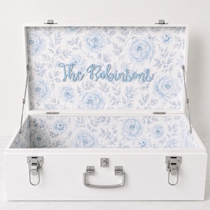 May include: A white wooden keepsake box with silver metal latches and a handle. The interior is lined with a light blue and white floral pattern. The text "The Robinsons" is mounted in blue script lettering on the inside of the lid.