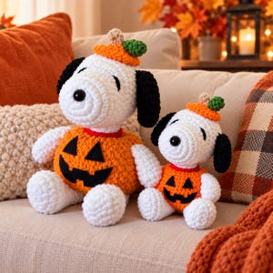 May include: Two white and black crocheted beagle figures wearing orange pumpkin costumes with black felt jack-o'-lantern faces and small green stems on their heads. The figures are crafted with textured yarn and feature black ears and noses.