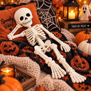 Op de afbeelding: Een gehaakt gebroken wit skeletfiguur met een schedel, borstkas en beweegbare ledematen. Het skelet rust tegen een oranje kussen met de zwarte tekst Spooky Vibes en een hartje, omringd door pompoenen en een zwarte spin.