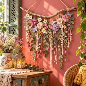 Puede incluir: Un tapiz decorativo con flores, hojas y mariposas de ganchillo suspendidas de una rama de madera natural. El arreglo incluye flores rosas, moradas y blancas con follaje verde y enredaderas colgantes, todo elaborado con texturas de hilo.