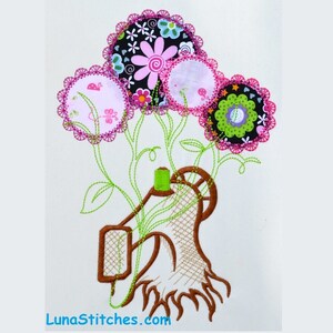 May include: Embroidered design of a sewing machine with three colorful flowers. The flowers are made of fabric scraps and have pink, green, and black accents. The sewing machine is brown and has a green spool of thread. The design is on a white background and includes the text "LunaStitches.com".