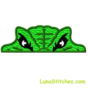 May include: Green embroidered patch with a pair of black eyes peeking out from behind a green scaly surface.