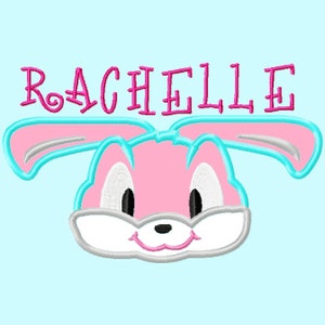Könnte beinhalten: Gesticktes Design mit einem rosa Hasengesicht mit hellblauen Umrissen und Akzenten. Der Name "RACHELLE" ist in Rosa über dem Hasen gestickt. Der Hintergrund ist hellblau.