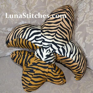 May include: A decorative pillow in the shape of a fleur-de-lis, with a tiger stripe pattern in black, white, and brown.