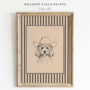 Puede incluir: Una lámina enmarcada con un dibujo a tinta negra de un perro con sombrero de vaquero sobre fondo beige. La lámina está bordeada por un marco de rayas negras y beige. El texto MEADOW FIELD PRINTS y Vintage Art aparece sobre el marco.