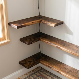 Peut inclure: Trois étagères d'angle en forme de L en bois brun foncé avec un grain visible. Chaque étagère présente une découpe circulaire près de l'angle, à travers laquelle un cordon noir passe verticalement, reliant les trois niveaux ensemble.
