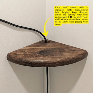 Puede incluir: Un estante de esquina triangular hecho de madera marrón oscura con un patrón de grano visible. El estante cuenta con un orificio circular para la gestión de cables, a través del cual pasa un cable negro. El texto en la imagen explica el orificio.