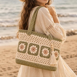 May include: A rectangular crochet tote bag featuring a pattern of square motifs with cream and sage green borders and light pink centers. The bag includes a solid sage green base, matching handles, and a decorative cream-colored tassel with wooden beads.