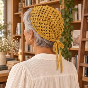 May include: A mustard yellow crochet headscarf featuring a diamond-shaped openwork pattern with a scalloped edge. The headscarf is secured at the back of the head with two long, thin crocheted ties that hang down, creating a simple and functional design.