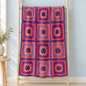 May include: A rectangular crochet blanket composed of twelve square motifs arranged in a grid. Each square features a central dark purple core surrounded by concentric rings of bright orange, pink, and purple yarn in a classic granny square pattern.