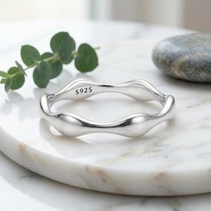 May include: A polished silver ring with a continuous wavy, organic band design. The interior of the band is clearly stamped with the text S925, indicating the metal composition. The ring features a smooth, reflective surface throughout its structure.