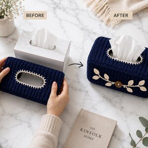 May include: A rectangular navy blue crochet tissue box cover featuring a cream-colored stitched border around the top opening and a decorative cream-colored leaf vine appliqué with a central brown wooden button on the front side of the cover.