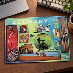 May include: A rectangular mousepad featuring a colorful comic-style illustration with the text AILMARY, AMAZE! AMAZE!, and RYAN GOSLING. The design includes scenes of an astronaut, a geodesic dome, a rocky landscape, and a robotic creature on a beach.