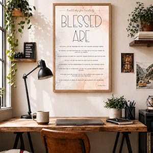 May include: A rectangular wall art print in a wooden frame featuring the text Beatitudes for Creativity, BLESSED ARE, and several lines of inspirational prose in black font against a soft, peach-toned watercolor background.