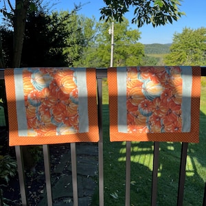 May include: Two rectangular fabric table runners featuring a central panel with a vibrant orange and light blue pumpkin print, bordered by solid orange fabric with a white polka dot pattern on the left and right edges of each runner.