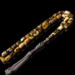 Peut inclure: Un chapelet composé de perles cylindriques couleur ambre moucheté avec des inclusions brun foncé. Le brin est relié par une pièce d'espacement en métal argenté au motif rayé texturé et se termine par un long pompon en métal argenté à brins multiples.