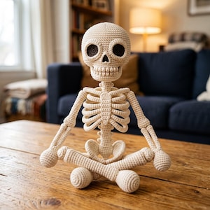 Pode incluir: Uma figura de esqueleto em crochê na cor creme, posada em uma posição de meditação sentada. A figura apresenta um crânio redondo com órbitas oculares circulares marrom-escuras, uma caixa torácica detalhada e membros articulados feitos de fio.