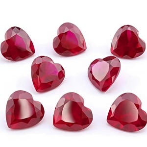 May include: Eight faceted heart-shaped gemstones in a deep, vibrant red color. Each stone features a polished surface with multiple geometric facets that reflect light, creating a brilliant appearance across the collection of loose red hearts.