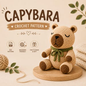 Op de afbeelding: Een gehaakt capybara-speeltje van lichtbruin garen met donkerbruine accenten op de snuit, oren en voeten, en een groene sjaal van garen gestrikt in een strik. De tekst CAPYBARA CROCHET PATTERN staat erboven met iconen voor PDF, beginners en cadeau.