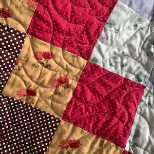 May include: A patchwork quilt featuring square fabric panels with various patterns including brown with white polka dots, solid bright pink with white dots, tan with red floral prints, and white with grey botanical illustrations, all joined by curved stitching.
